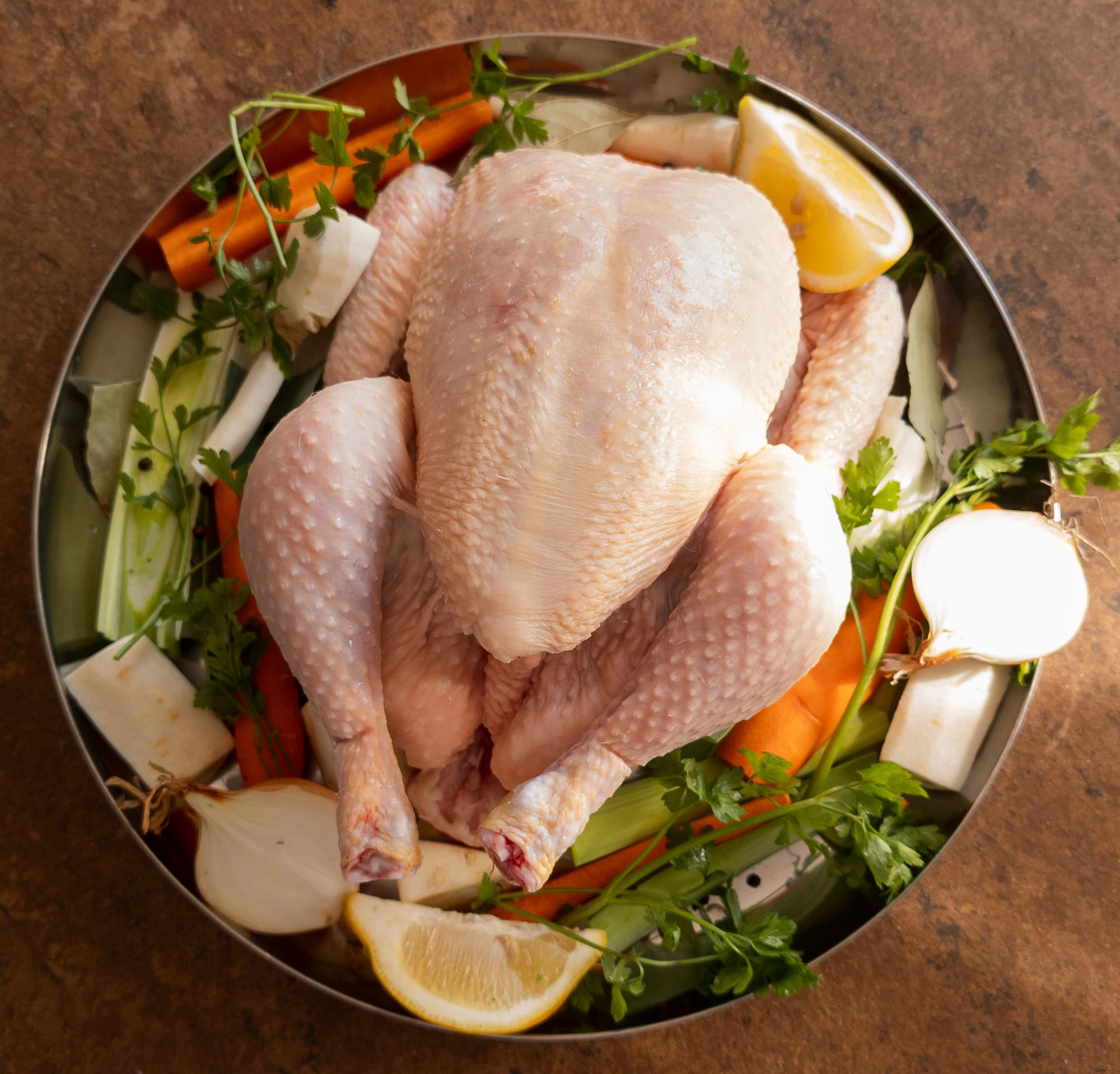 Ein ganze rohes Hähnchen mit Suppengrün auf einer runden Platte angerichtet