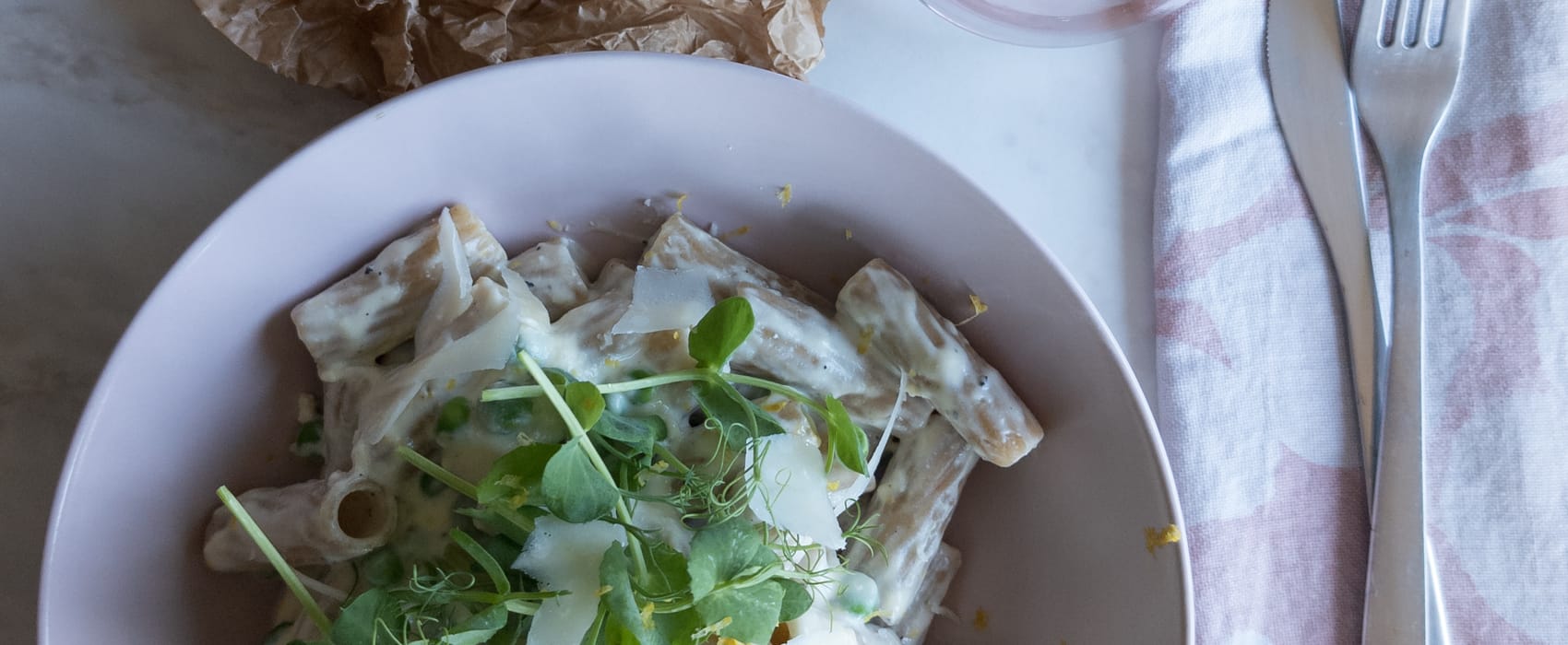 Schüssel mit Vollkornnudeln, Erbsen-Ricotta-Soße, garniert mit Erbsensprossen, Parmesan und Zitrone