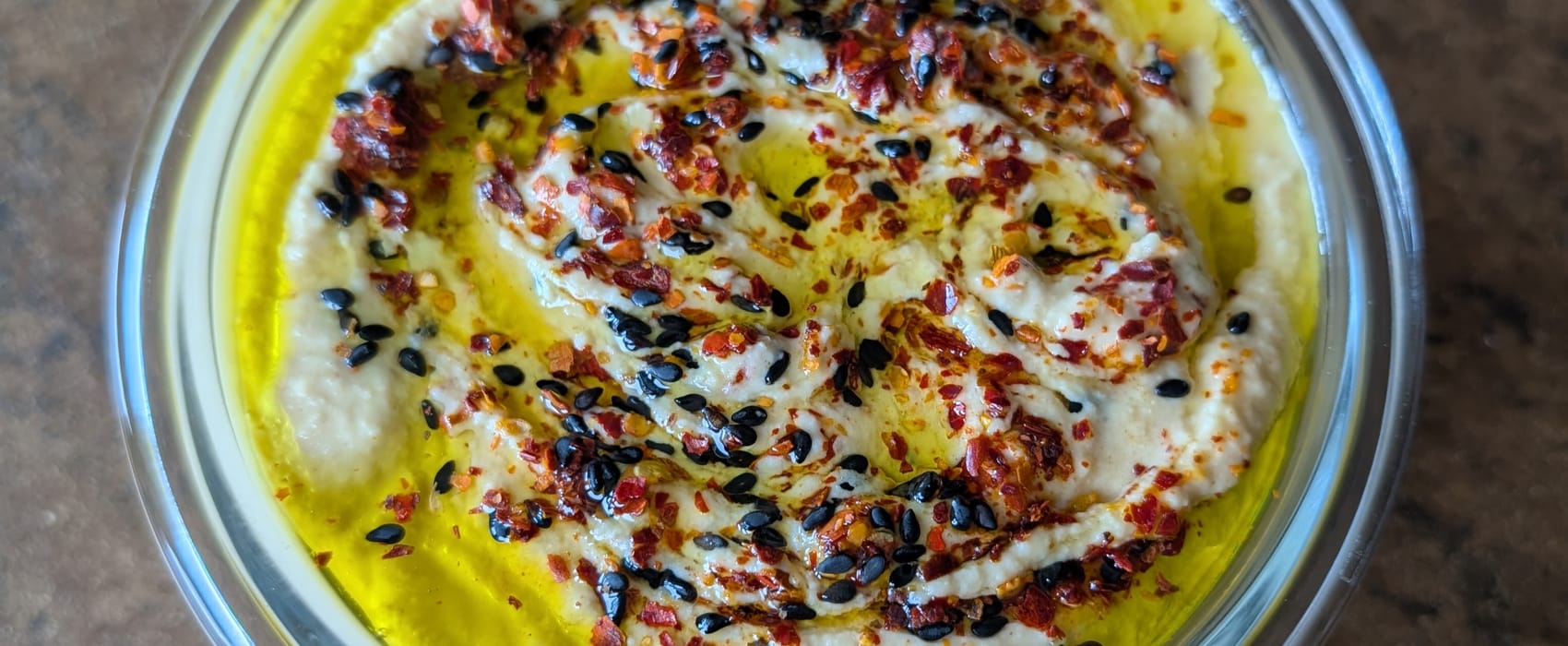 Eine Schale mit cremigem Hummus garniert mit Olivenöl, Chiliflocken und schwarzen und weißen Sesam